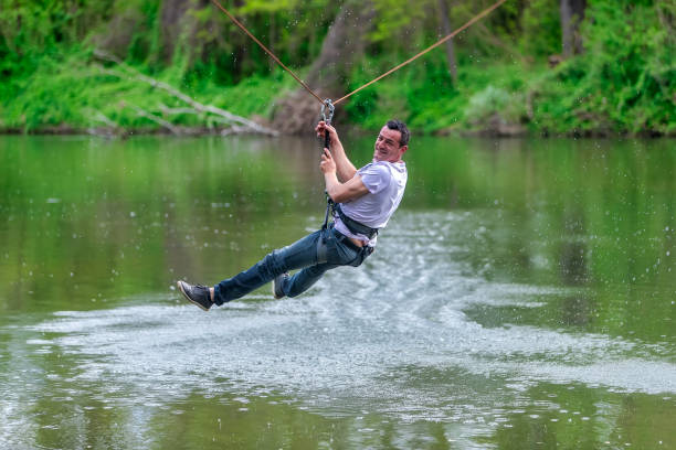 young man flying down on zipline over the river, extreme sport